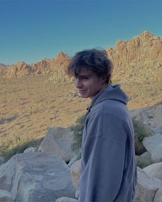 a young man standing on top of a rocky hillside next to mountains in the distance