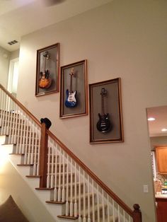 three guitars hanging on the wall next to a stair case in a house with white railings