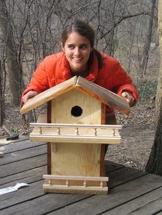 a woman in an orange jacket holding up a birdhouse