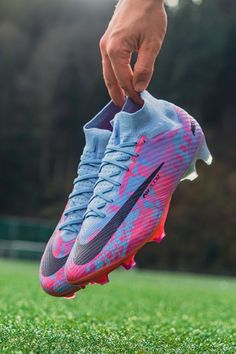 a person tying the shoe laces on a soccer boot in a field with trees in the background