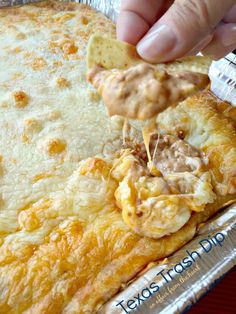 a person is dipping some food into a foil pan filled with cheesy bread