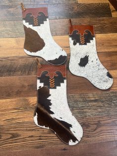 two pairs of cowhide socks with brown and white designs on them sitting on a wooden floor