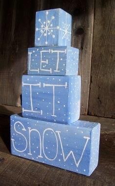 three wooden blocks with the words let it snow written in white paint on them, stacked up against a wood background