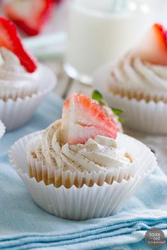 some cupcakes with white frosting and strawberries on top are sitting on a blue towel