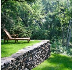 a wooden bench sitting on top of a stone wall in the middle of a forest