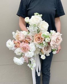 a woman holding a bouquet of white and pink flowers in front of a gray wall