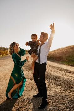 a man, woman and child standing in the middle of a dirt road at sunset