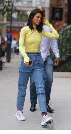 a woman in yellow shirt and jeans walking down the street