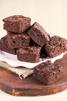 chocolate brownies stacked on top of each other in front of a wooden cutting board