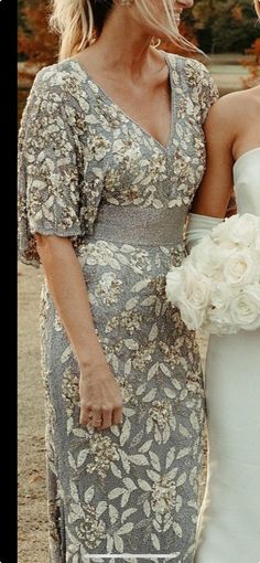 two women in dresses are walking side by side and one is holding a flower bouquet