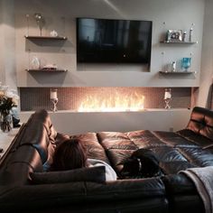 a woman laying on top of a leather couch in front of a flat screen tv