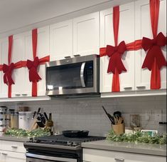 a kitchen decorated for christmas with red bows on the wall and white cabinets, along with an oven