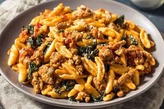 a plate full of pasta with meat and spinach on it next to a glass of milk