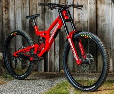 a red mountain bike parked in front of a wooden fence