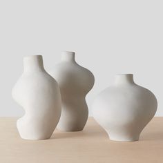 three white vases sitting on top of a wooden table