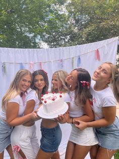 a group of young women standing next to each other in front of a white cake