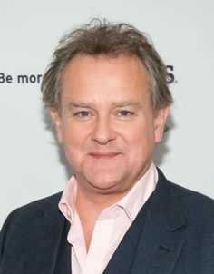 a man in a suit and pink shirt poses for the camera on a red carpet