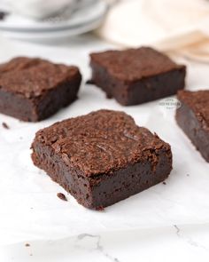 four pieces of brownie sitting on top of a white paper covered counter next to a cup and saucer