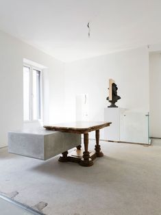 an empty room with a table in the middle and a sculpture on the far wall