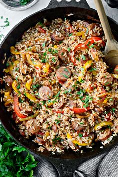 a skillet filled with rice, sausage and veggies on top of a table