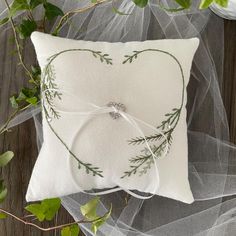 a white pillow with greenery on it and a ribbon tied around the edge, sitting on a wooden surface