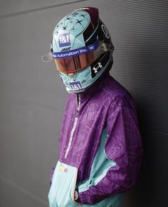 a person wearing a purple jacket and helmet standing next to a wall with his hands on his hips