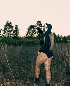 a woman wearing a mask and fishnet stockings is standing in the tall grass with her mouth open