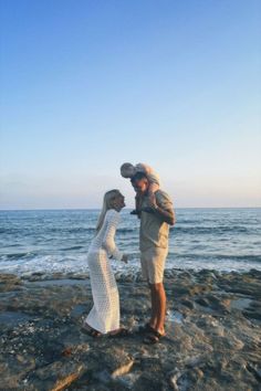 a man and woman standing on top of a rocky beach next to the ocean holding a baby