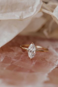 a diamond ring sitting on top of a pink marble table next to a white cloth