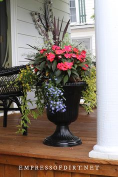 a large black vase filled with flowers sitting on top of a wooden porch next to a white house