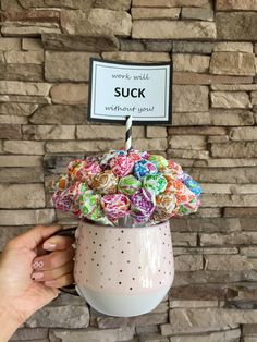 a person holding a cup filled with colorful candies in front of a brick wall