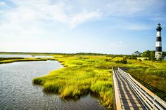 a boardwalk leading to a light house in the distance with water and grass around it