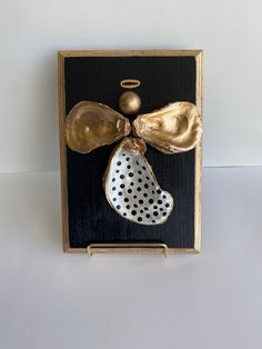 a black and gold plaque with a polka dot boot on it's side, decorated with an angel ornament