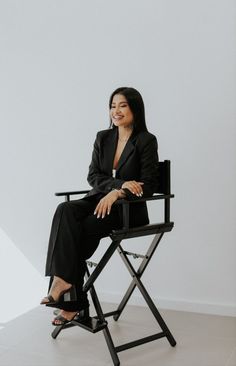 a woman sitting on top of a black chair in front of a white wall and smiling