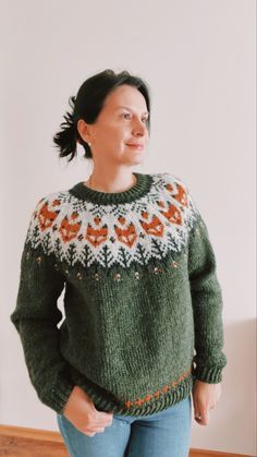 a woman standing in front of a wall wearing a green sweater