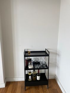 a shelf with wine glasses and bottles on it in a white walled room next to a wooden floor