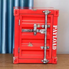 a red box with metal handles and latches on the bottom is sitting on a wooden table