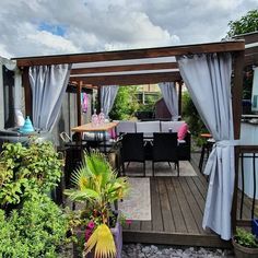 an outdoor dining area with patio furniture and curtains on the outside, surrounded by greenery