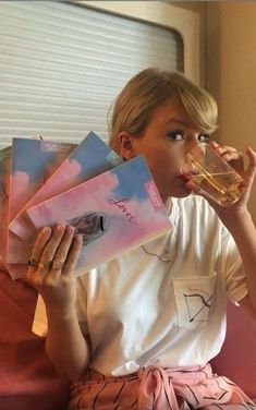 a woman sitting on a couch drinking out of a glass while holding papers in front of her face