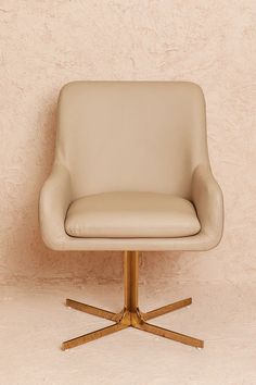 a beige leather chair sitting in front of a wall with a wooden base and gold legs