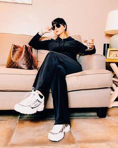 a woman sitting on top of a couch next to a purse and holding a drink