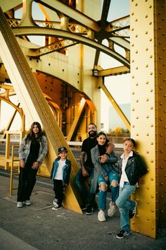 a group of people standing next to each other near a yellow metal structure on a bridge