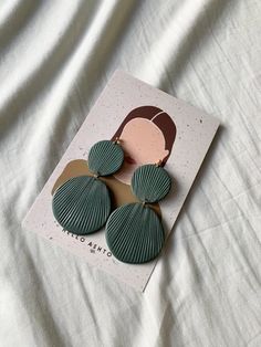 a pair of green fan - shaped earrings on top of a white sheet with a brown background