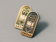 two gold colored pins with an image of a hand holding a beer bottle and the word smash on it