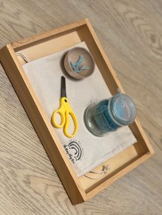 a pair of yellow scissors sitting on top of a wooden box next to a cup