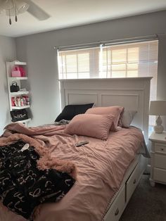 a bed with pink comforter and pillows in a bedroom next to a book shelf