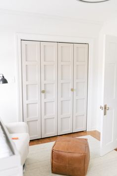 a living room with white walls and leather footstool in front of the doors