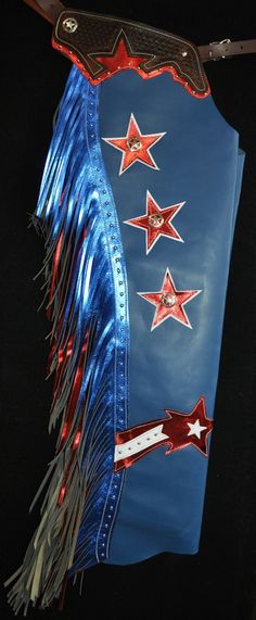 Custom Chaps, Handmade in the U.S.A.! These chaps are made with a quality, blue chap leather. They have 8 oz. tooling leather trim pieces, dyed a dark brown with a basket weave tooled stamp on them, star cut out, and metallic red backing. There is 14" metallic blue and red double fringe on the leg, bordered with metal studs. The legs are accented with metallic red stars and centered with star conchos. These chaps close with full zippers. They are a nice choice for work or show. Please message us Diy Chaps From Jeans, Sequin Chaps, Custom Chaps, Rodeo Chaps, Shotgun Chaps, Double Fringe, Star Cut Out, Red Fringe, Red Stars