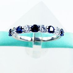 a white gold ring with blue and clear stones on it's side, sitting on top of a green cloth