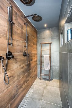 a walk in shower sitting next to a wooden wall and tiled floor with two hand held shower heads